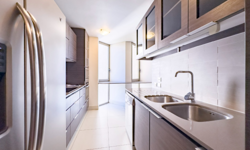 Cocina moderna con mobiliario de madera, lavaplatos doble y luz natural al fondo.